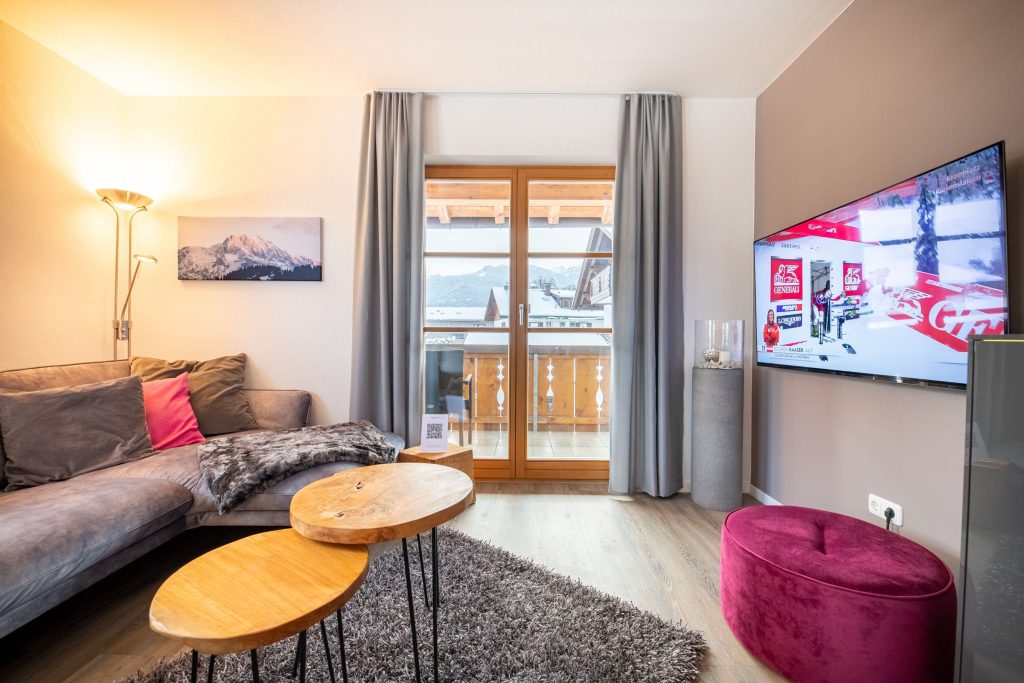 Wohnzimmer mit einem Stoffhocker und Fernseher in Ferienwohnung in Garmisch-Partenkirchen