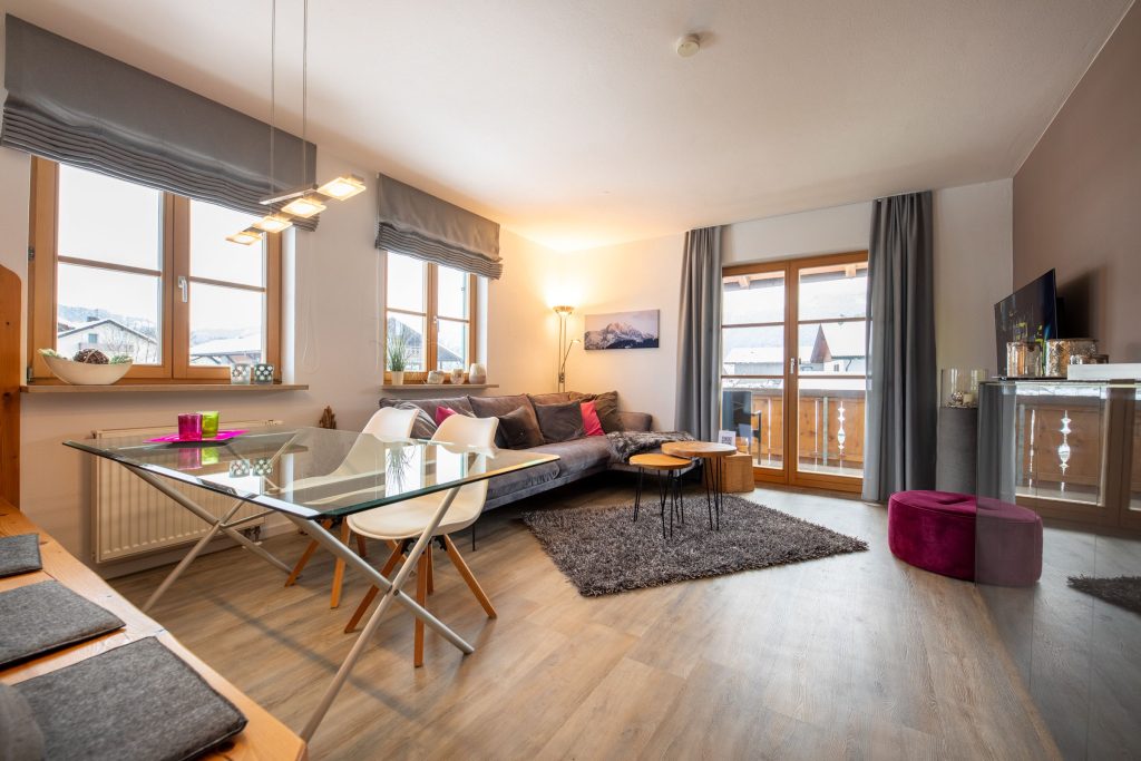 Wohnzimmer und Esszimmer mit Glastisch und grauem Sofa in Ferienwohnung in Garmisch-Partenkirchen