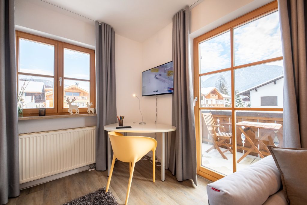 Wohnzimmer mit einem kleinen Tisch mit einem Stuhl, einem Fernseher und einem Ausgang zu dem Balkon in Ferienwohnung in Garmisch-Partenkirchen