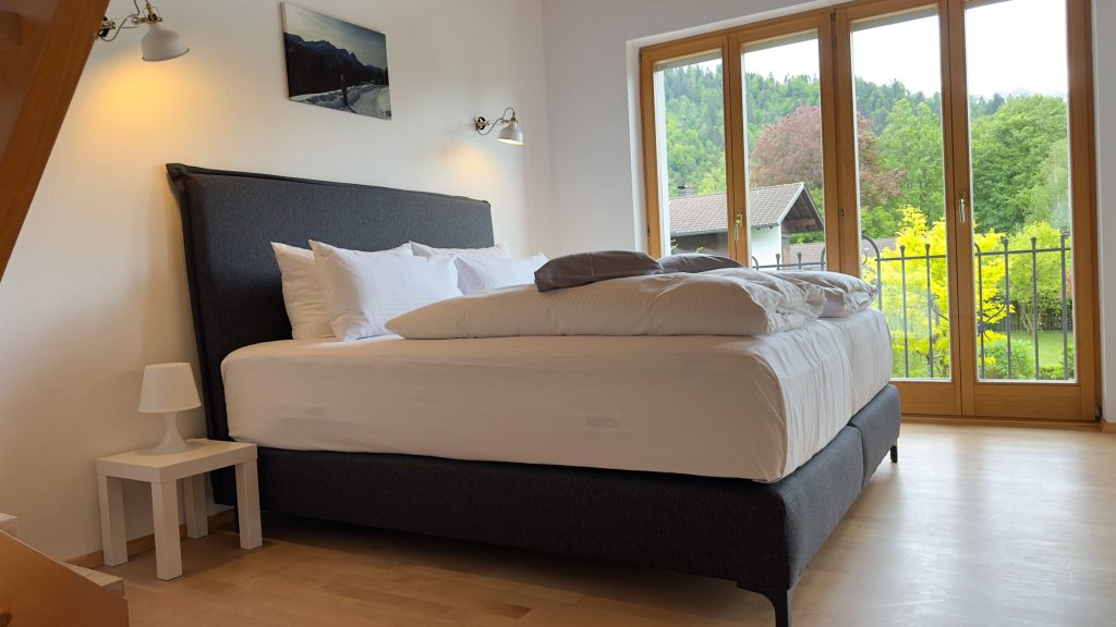 Boxspringbett mit Ausblick auf den grünen Garten in Ferienwohnung in Garmisch-Partenkirchen 