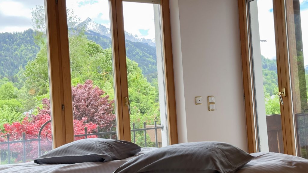 Schlafbett mit großen Fenstern in Ferienwohnung in Garmisch-Partenkirchen