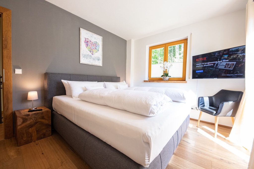 Doppelbett mit Fernseher und Stuhl in Ferienwohnung in Garmisch-Partenkirchen