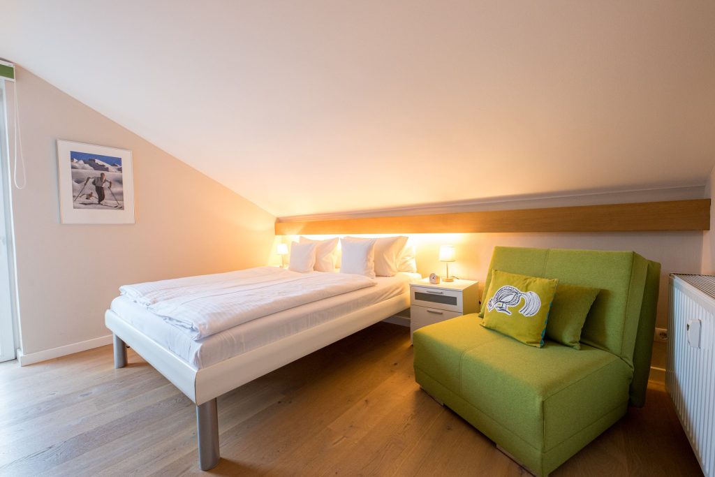 Schlafzimmer mit grünem Sessel und weißem Bett in Ferienwohnung in Garmisch-Partenkirchen