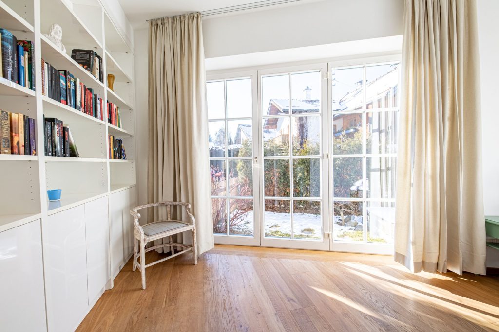 Fensterfront mit creme farbenen Vorhängen und einem kleinen Stuhl in Ferienwohnung in Garmisch-Partenkirchen