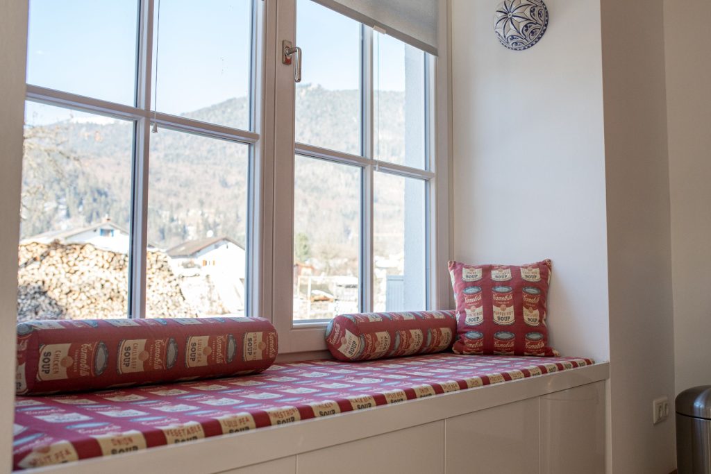 Sitzmöglichkeit mit Kissen an einem großen Fenster mit Ausblick in Ferienwohnung in Garmisch-Partenkirchen