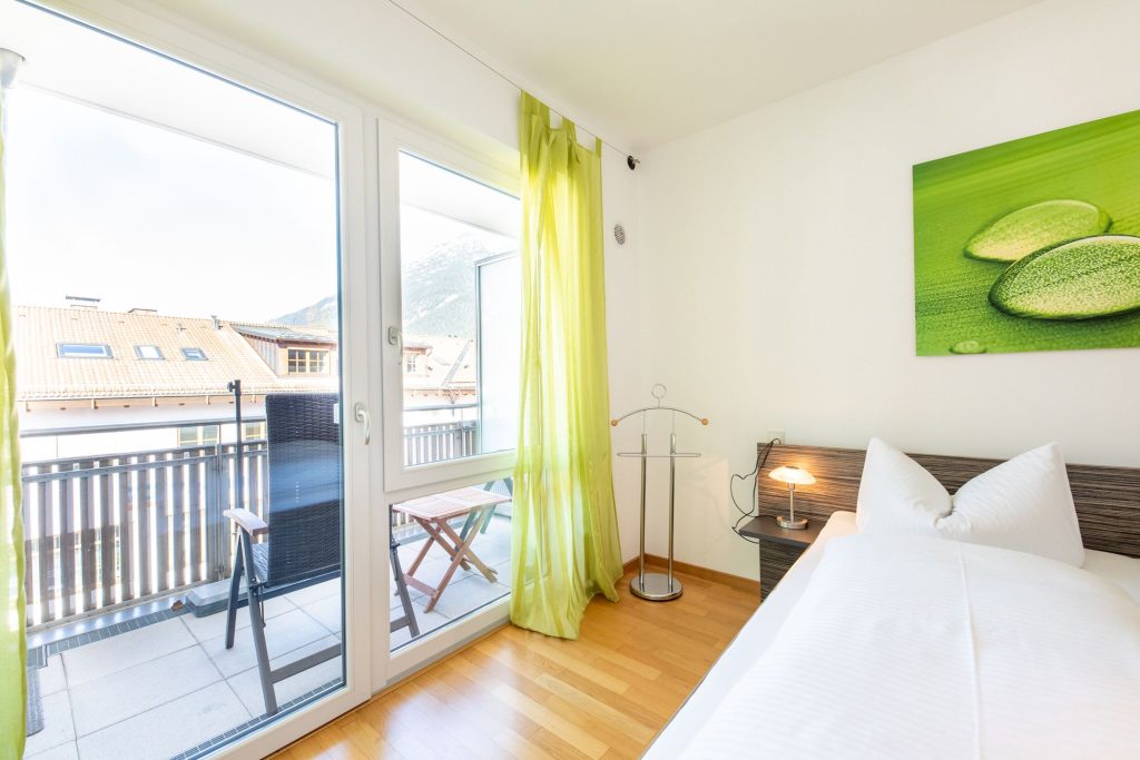 Bett mit grünem Bild und hellgrünen Gardinen in Ferienwohnung in Garmisch-Patenkirchen